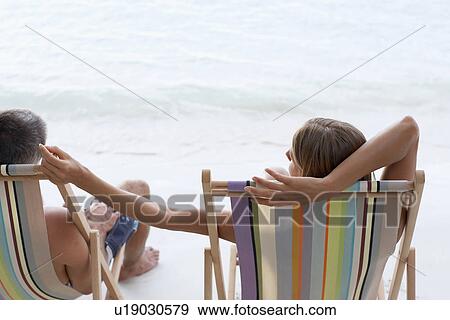Mid adult couple on lounge chairs on beach View Large Photo Image Stock Photo - Mid adult couple on lounge chairs on beach. Fotosearch