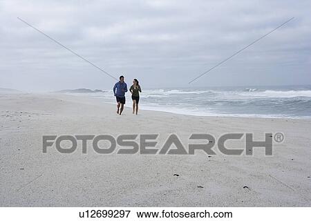 Stock Photo - Mid adult couple running on sandy beach, Cape Town, South Africa. Fotosearch