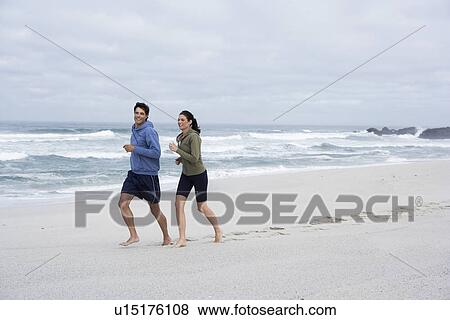 Stock Photo - Mid adult couple running on sandy beach, Cape Town, South Africa. Fotosearch