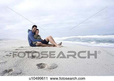 Stock Image - Mid adult couple sitting on sandy beach, Cape Town, South Africa. Fotosearch