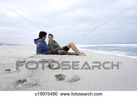 Stock Image - Mid adult couple sitting on sandy beach, Cape Town, South Africa. Fotosearch