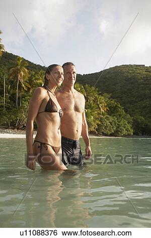 Stock Photograph - Mid adult couple standing in water near beach, St John, US Virgin Islands, USA. Fotosearch