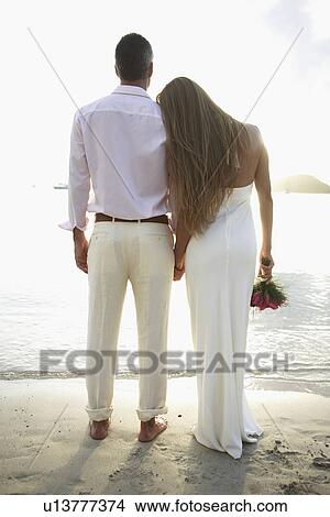 Picture - Newlyweds looking at view on beach (rear view). Fotosearch
