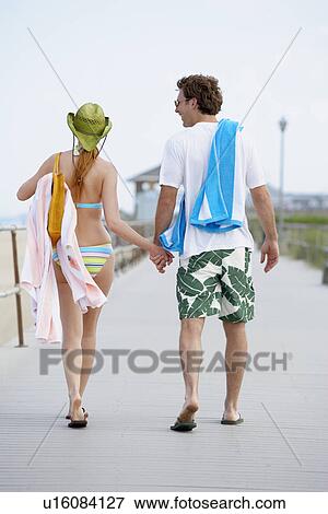 Young couple in beach attire walking and holding hands (rear view) View Large Photo Image Stock Photo - Young couple in beach attire walking and holding hands (rear view). Fotosearch