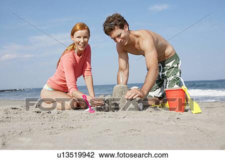 Stock Image - Young couple making sandcastle. Fotosearch