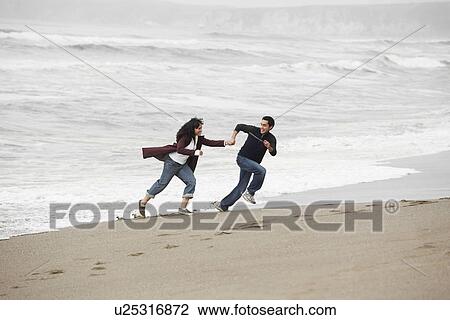 Stock Image - Young couple running on sandy beach. Fotosearch
