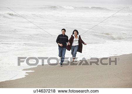 Stock Photo - Young couple running on sandy beach. Fotosearch