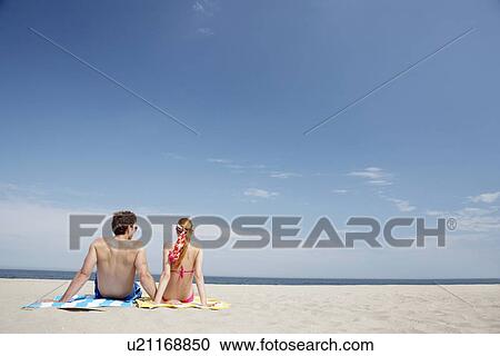 Stock Image - Young couple sitting at beach and looking at view (rear view), Spring Lake, New Jersey, USA. Fotosearch