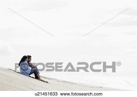 Young couple sitting on sandy beach View Large Photo Image Stock Image - Young couple sitting on sandy beach. Fotosearch