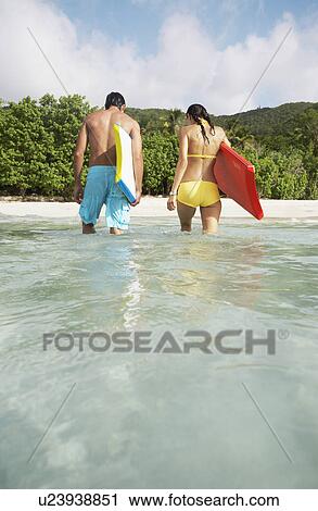 Stock Image - Young couple with bodyboards walking in ocean, St John, US Virgin Islands, USA. Fotosearch