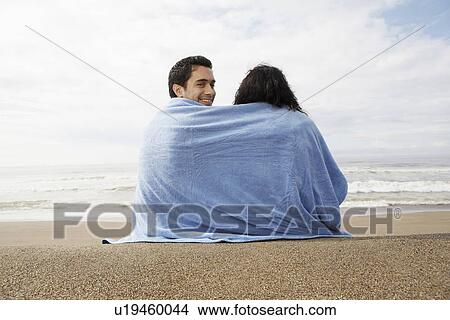 Young couple wrapped in towel on beach (rear view) View Large Photo Image Picture - Young couple wrapped in towel on beach (rear view). Fotosearch