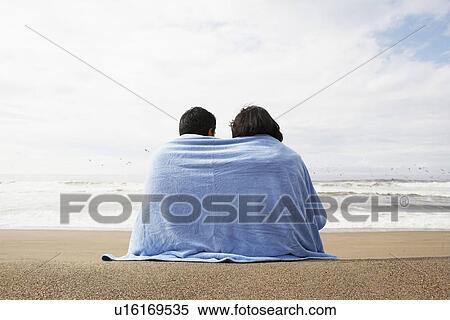 Stock Photography - Young couple wrapped in towel on beach (rear view). Fotosearch