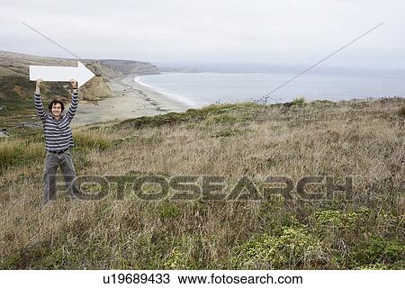 Stock Image - Man holding direction arrow near beach. Fotosearch