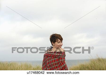 Stock Image - Woman sitting on beach (portrait, rear view). Fotosearch