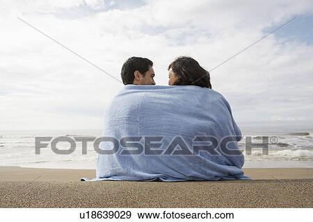 Stock Photo - Young couple wrapped in towel on beach (rear view). Fotosearch