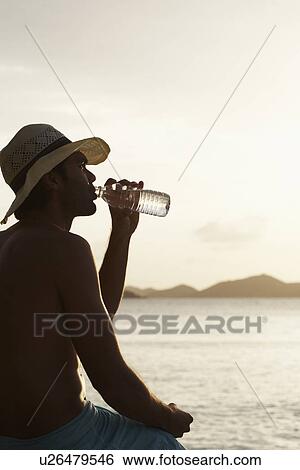 Young man drinking water on beach View Large Photo Image Stock Photograph - Young man drinking water on beach. Fotosearch