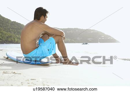 Young man sitting on surfboard on beach, St. John, US Virgin Islands, USA View Large Photo Image Stock Image - Young man sitting on surfboard on beach, St. John, US Virgin Islands, USA. Fotosearch