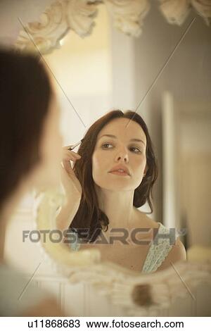 Stock Image - Woman applying make-up in front of mirror. Fotosearch