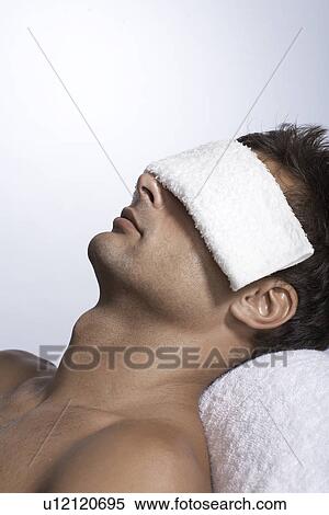 Stock Photography - Mid adult man lying with towel over eyes. Fotosearch