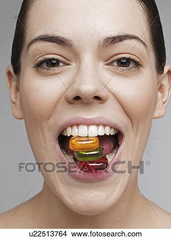 Picture - Young woman holding candies in teeth. Fotosearch
