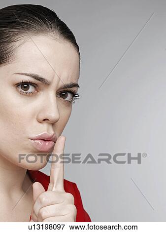Stock Photo - Young woman holding finger on lips. Fotosearch
