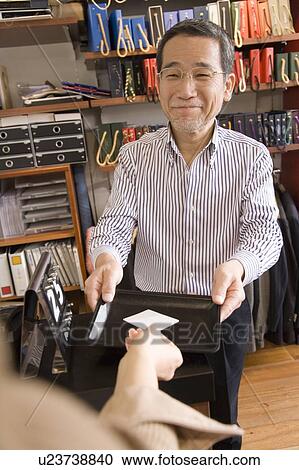 Stock Image - A Mature Adult Man Taking a Customer's Credit Card, Front View. Fotosearch