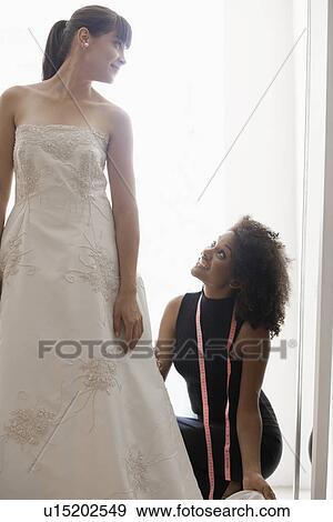 Stock Photo -  Woman adjusting bride's wedding dress. Fotosearch
