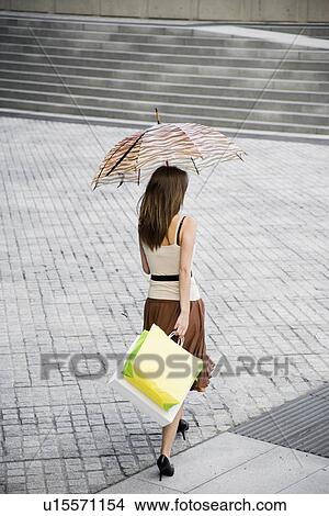 Picture - Woman with umbrella and shopping bags walking across public square (rear view, high angle view). Fotosearch