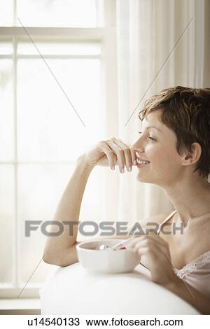 Stock Image - Mid adult woman eating breakfast. Fotosearch