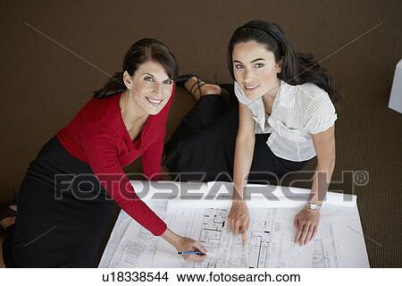 Two businesswomen examining blueprints (portrait, high angle view) View Large Photo Image Picture - Two businesswomen examining blueprints (portrait, high angle view). Fotosearch