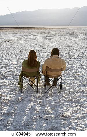 Stock Image - Couple Sitting on Sun Loungers in Desert. Fotosearch