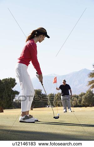Stock Image - Woman playing golf, man holding golf flag. Fotosearch