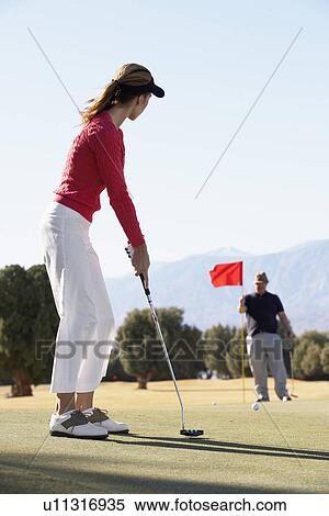 Stock Photography - Woman playing golf, man holding golf flag. Fotosearch