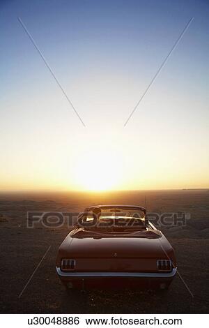 Stock Photograph - Young man looking at sunset in convertible, Arizona, USA. Fotosearch
