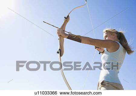 Stock Photograph - Young woman arrow shooting (low angle view). Fotosearch