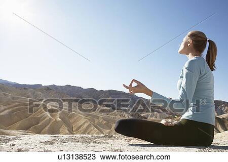Stock Image - Young woman in lotus position in desert. Fotosearch