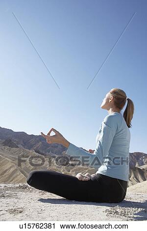 Stock Image - Young woman in lotus position in desert. Fotosearch