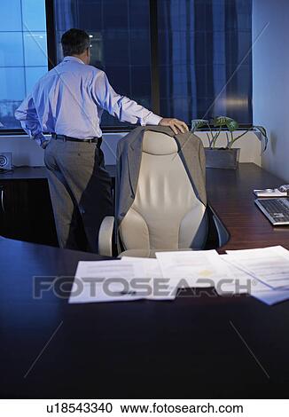 Stock Image - Businessman Standing by Desk and Working Late. Fotosearch