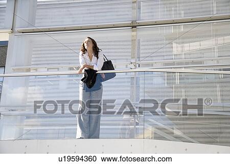 Stock Image - Businesswoman leaning on railing (low angle view). Fotosearch