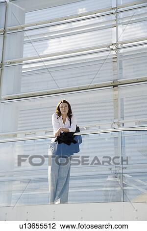 Stock Image - Businesswoman leaning on railing (portrait, low angle view). Fotosearch