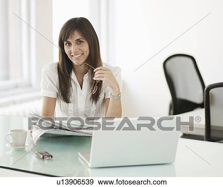 Stock Photo - Businesswoman Reading Newspaper at Desk. Fotosearch