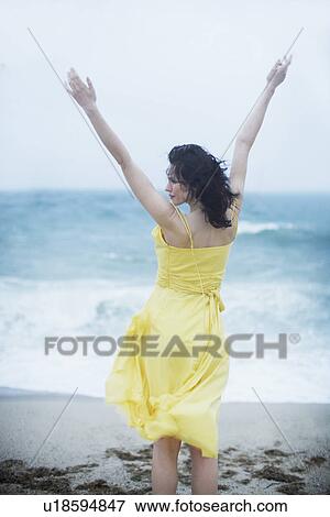 Stock Photo - Young woman raising hands on beach. Fotosearch