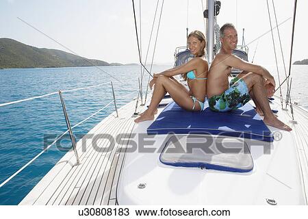 Stock Image - Mid adult couple on sailboat. Fotosearch