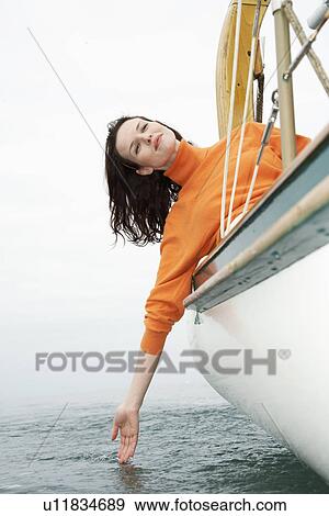 Stock Photo - Young woman leaning over boat side, touching water (low angle view). Fotosearch