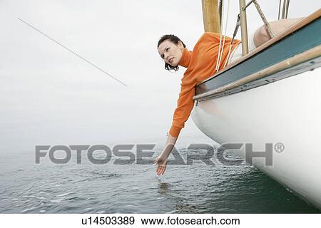 Stock Photo - Young woman leaning over boat side, touching water (low angle view). Fotosearch