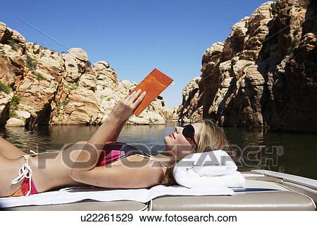 Stock Photo - Young woman reading book in motorboat. Fotosearch