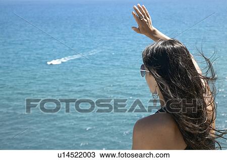 Stock Image - Young Woman Waving at Boat. Fotosearch