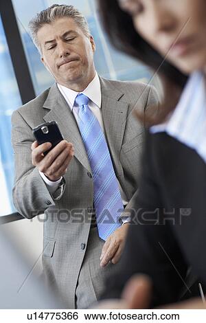 Businessman checking mobile phone near colleague View Large Photo Image Stock Photograph - Businessman checking mobile phone near colleague. Fotosearch