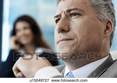 Stock Photo - Businessman Thinking, Woman on Phone in Background. Fotosearch