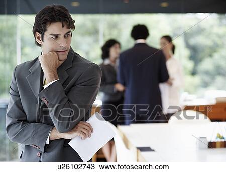 Businessman with documents thinking, colleagues in background View Large Photo Image Stock Image - Businessman with documents thinking, colleagues in background. Fotosearch